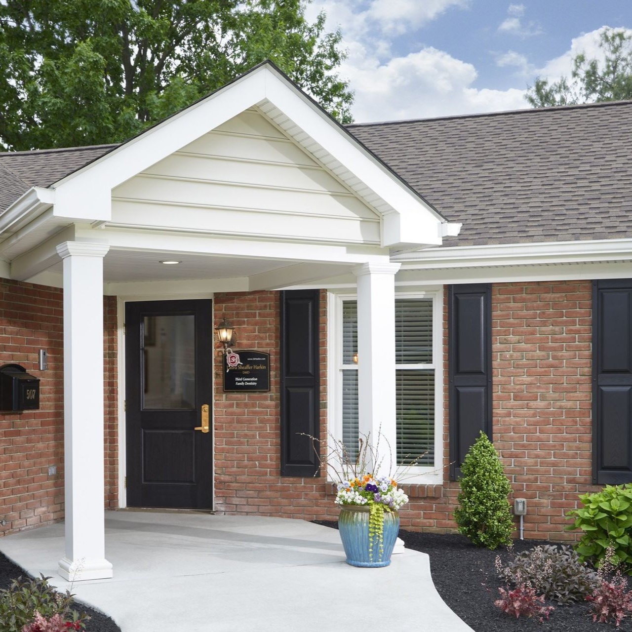 Brick house entrance with white porch, black doors, and potted flowers