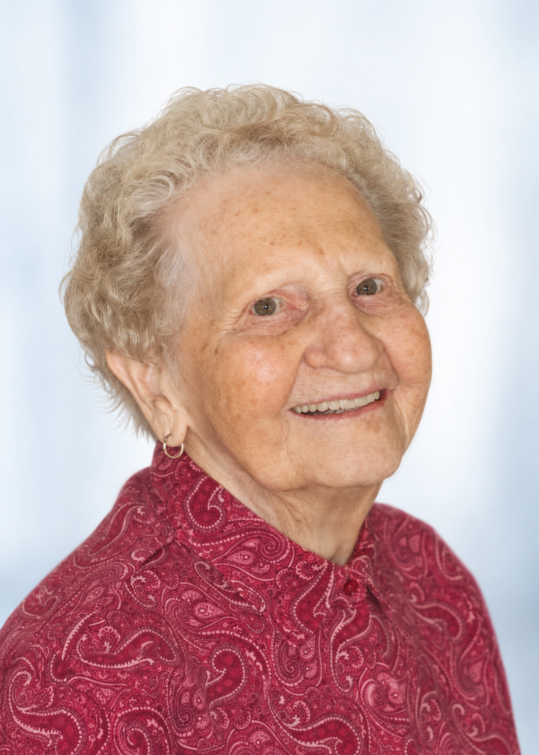 Smiling elderly woman in a red patterned blouse against a light blue background