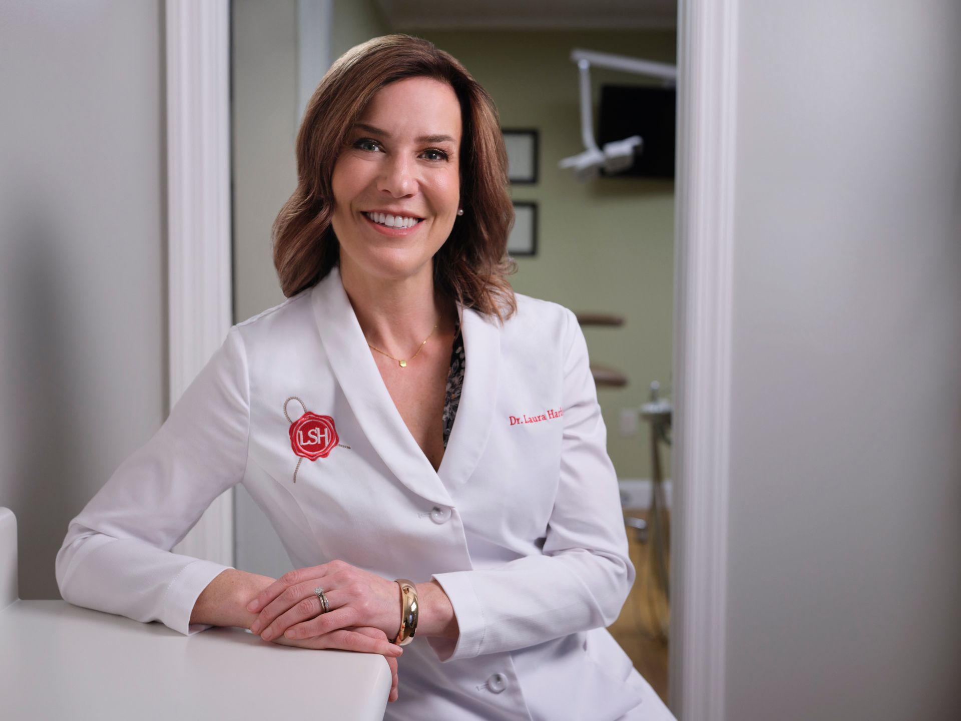 Smiling doctor in a white coat seated at a desk in a clinical office