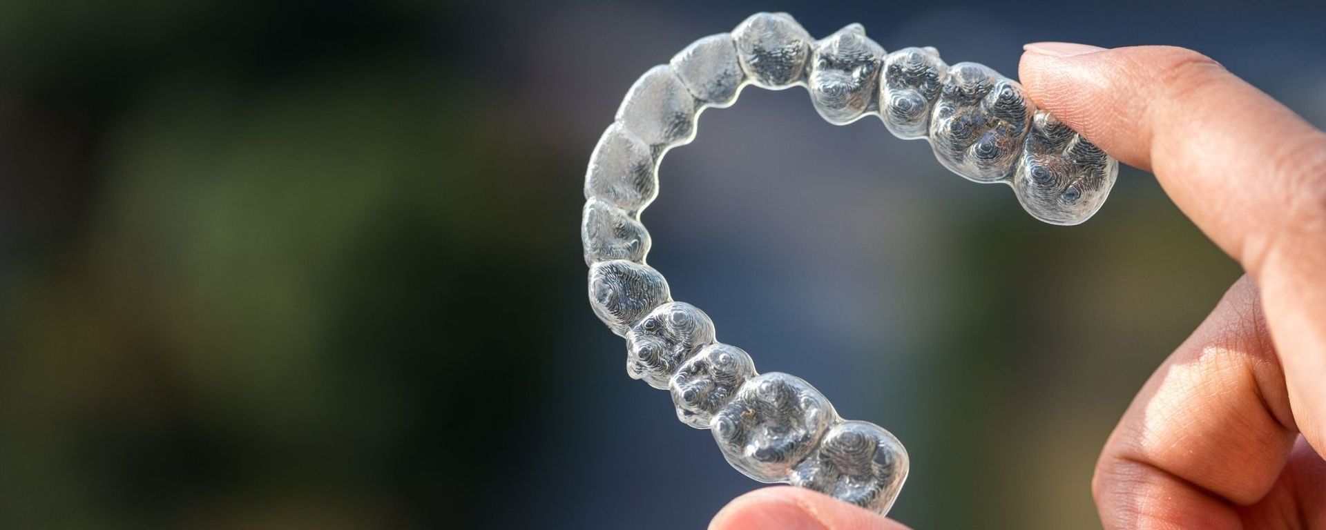 Hand holding a clear aligner against a blurred green background