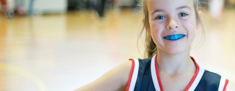 Smiling child with blue mouthguard in a basketball uniform on an indoor court