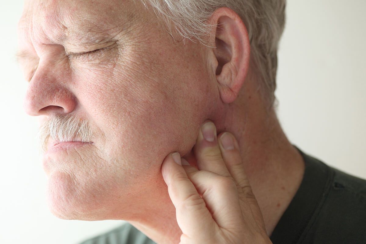 Close-up of a person holding their neck, eyes closed in pain or discomfort