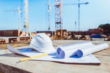 Un casco, planos y un lápiz están sobre una mesa en un sitio de construcción.