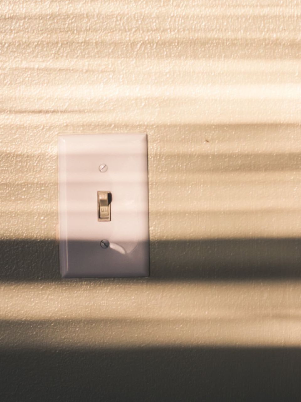 Light switch on a wall a light switch on a wall with a shadow on it .