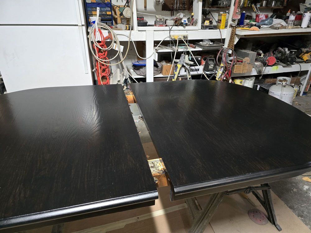 Two black tabletop panels in a workshop, separated by a narrow gap, with tools and shelves in the background.
