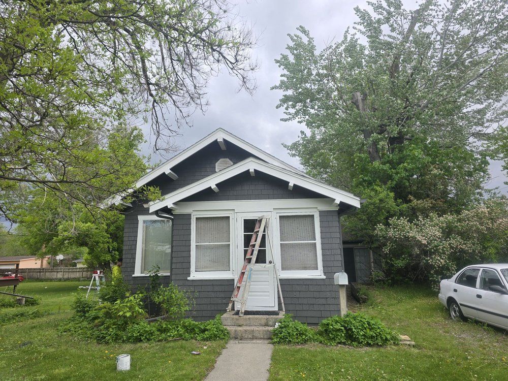 Small gray house with a white front door, front steps, and trees in the yard