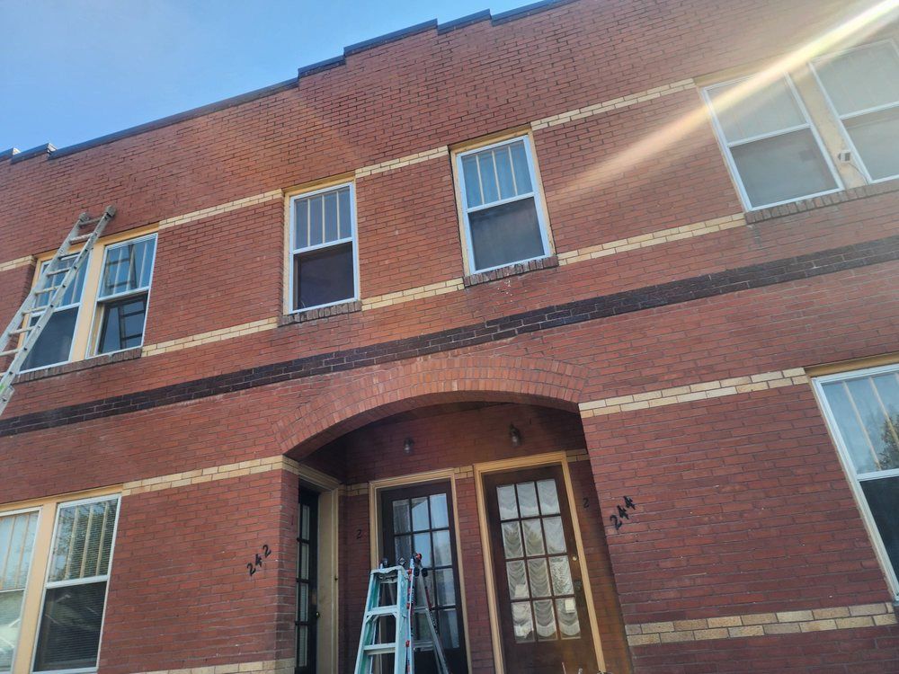 Brick building facade with arched wooden door and several windows under bright sun flare
