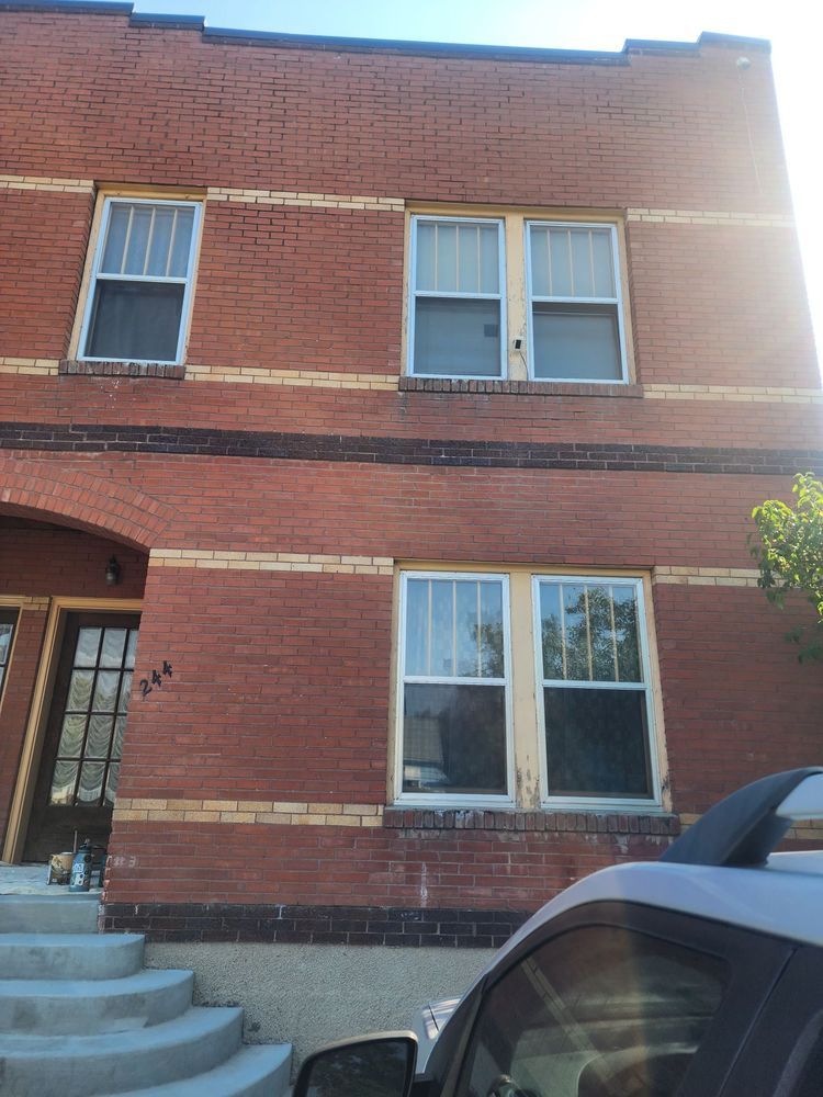 Red brick townhouse facade with white-trimmed windows, front steps, and a parked car in the foreground
