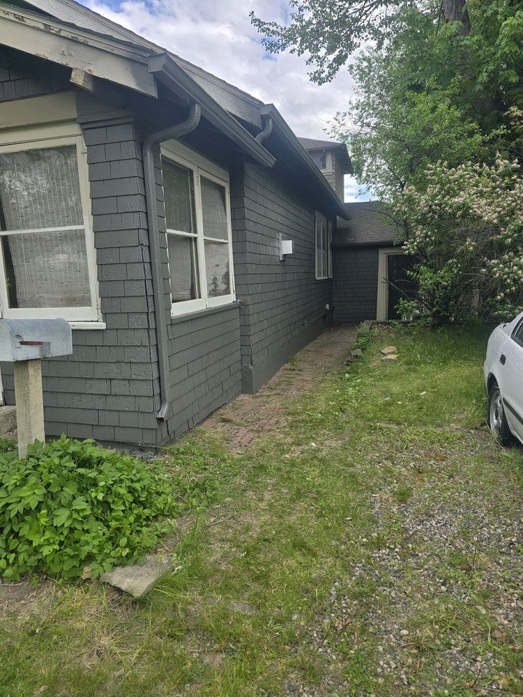 Gray house side yard with grass path, windows, and a parked white car