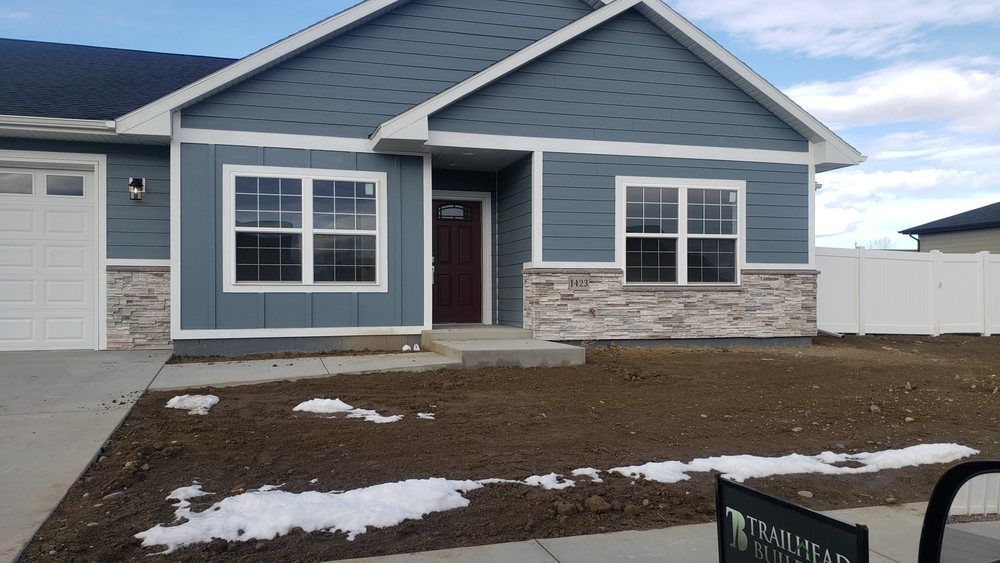 Single-story gray house with stone siding, a front porch, and patches of snow in the yard.