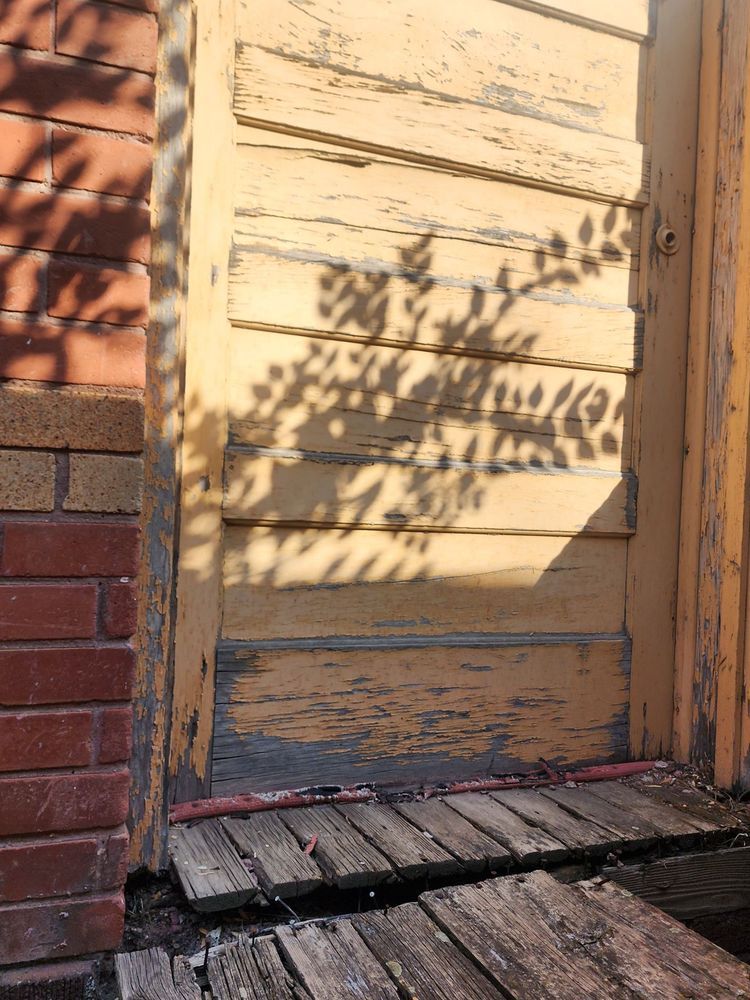 Weathered yellow door beside a brick wall, with leaf shadows across it and a worn wooden step below