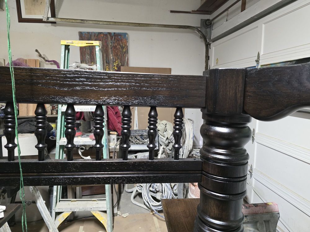 Close-up of a dark wooden staircase railing with turned balusters in a workshop or garage.