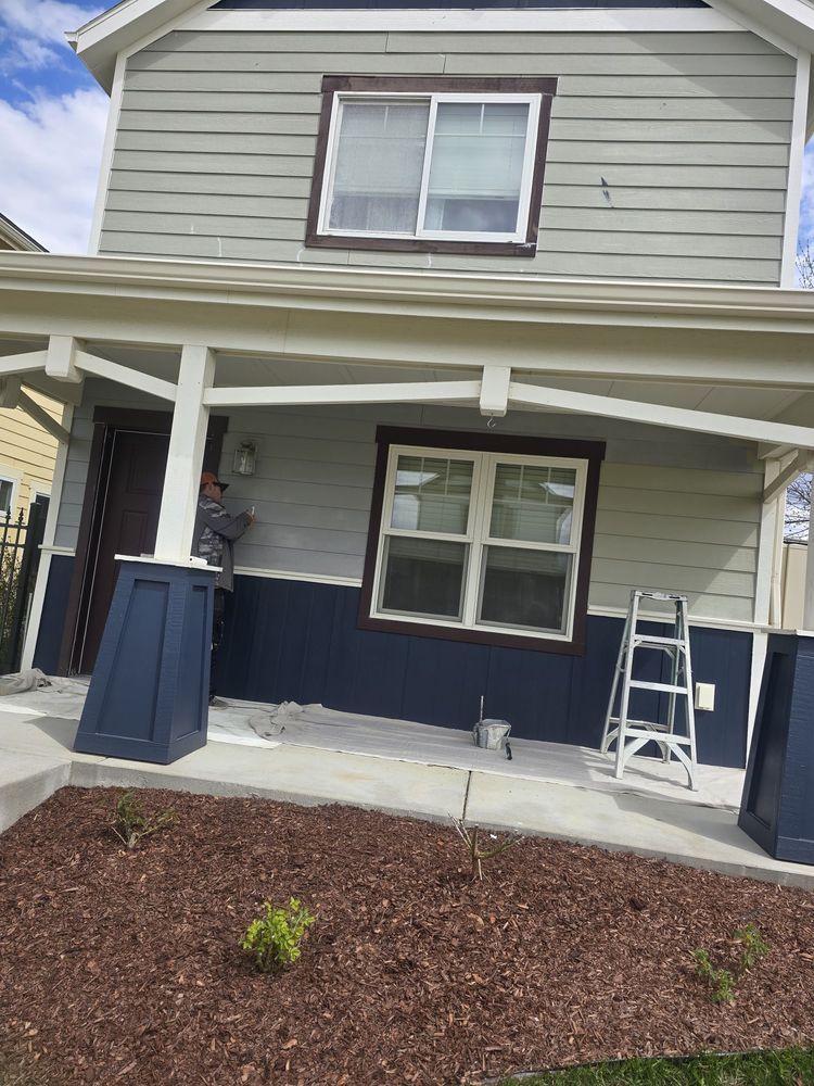 Front of a two-story house with gray siding, navy porch posts, and a white ladder on the porch.