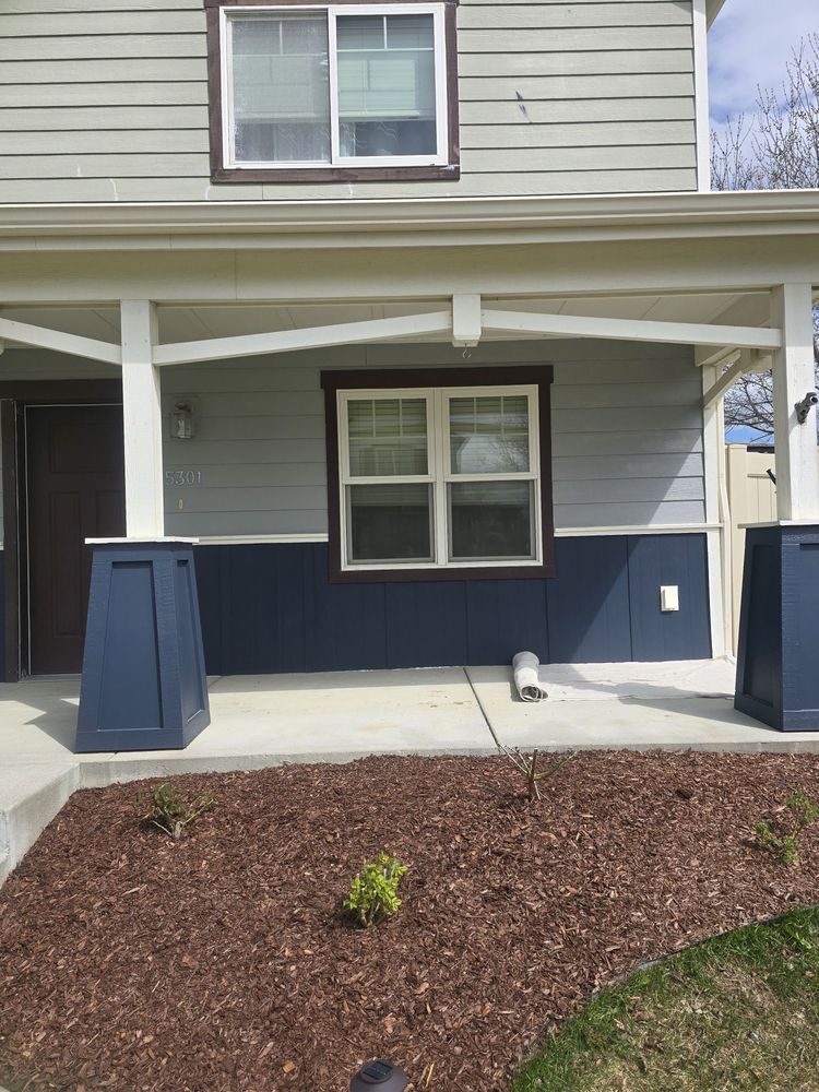 Front porch of a house with gray siding, blue trim, and a mulched front bed.