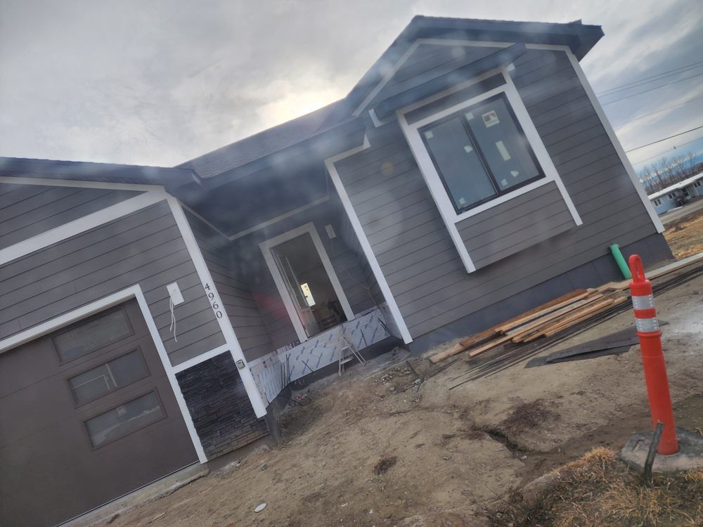 Gray house under construction with garage, front entry, and orange traffic cone in a dirt driveway