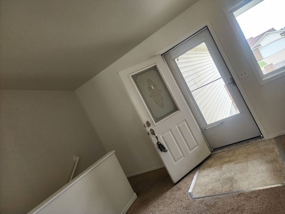 Tilted view of an open front door with a white rug in a sparsely furnished entryway