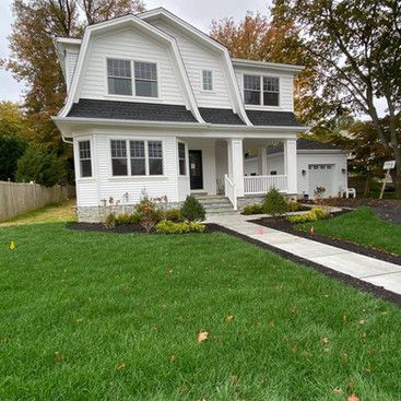 a white house with a black roof and a large lawn in front of it .