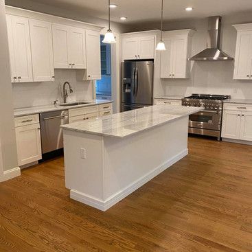 a kitchen with white cabinets , stainless steel appliances , hardwood floors and a large island .