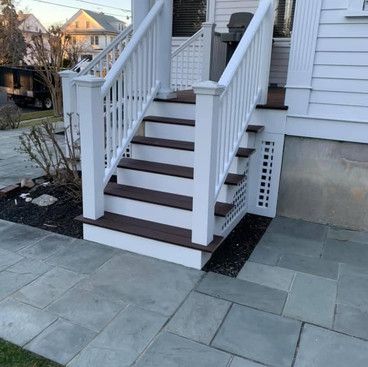 a white porch with wooden stairs and a white railing .