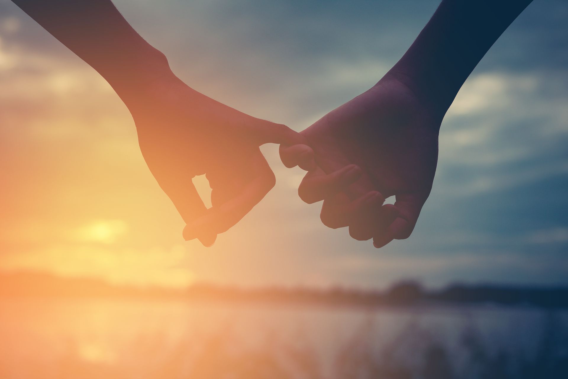 Two hands holding at sunset over a blurred water horizon