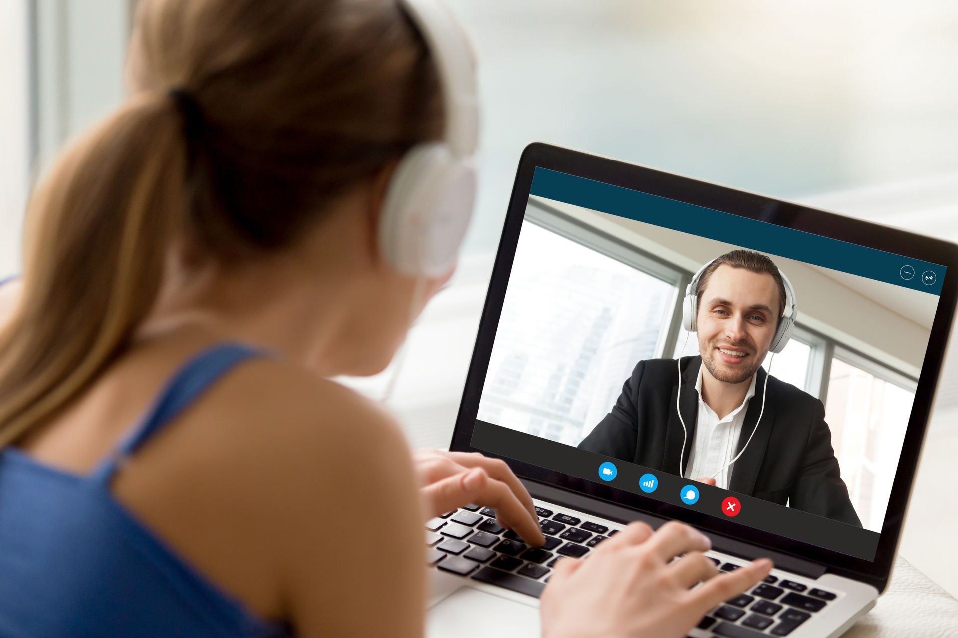 Woman on a laptop video call with a man, typing in a bright home office.