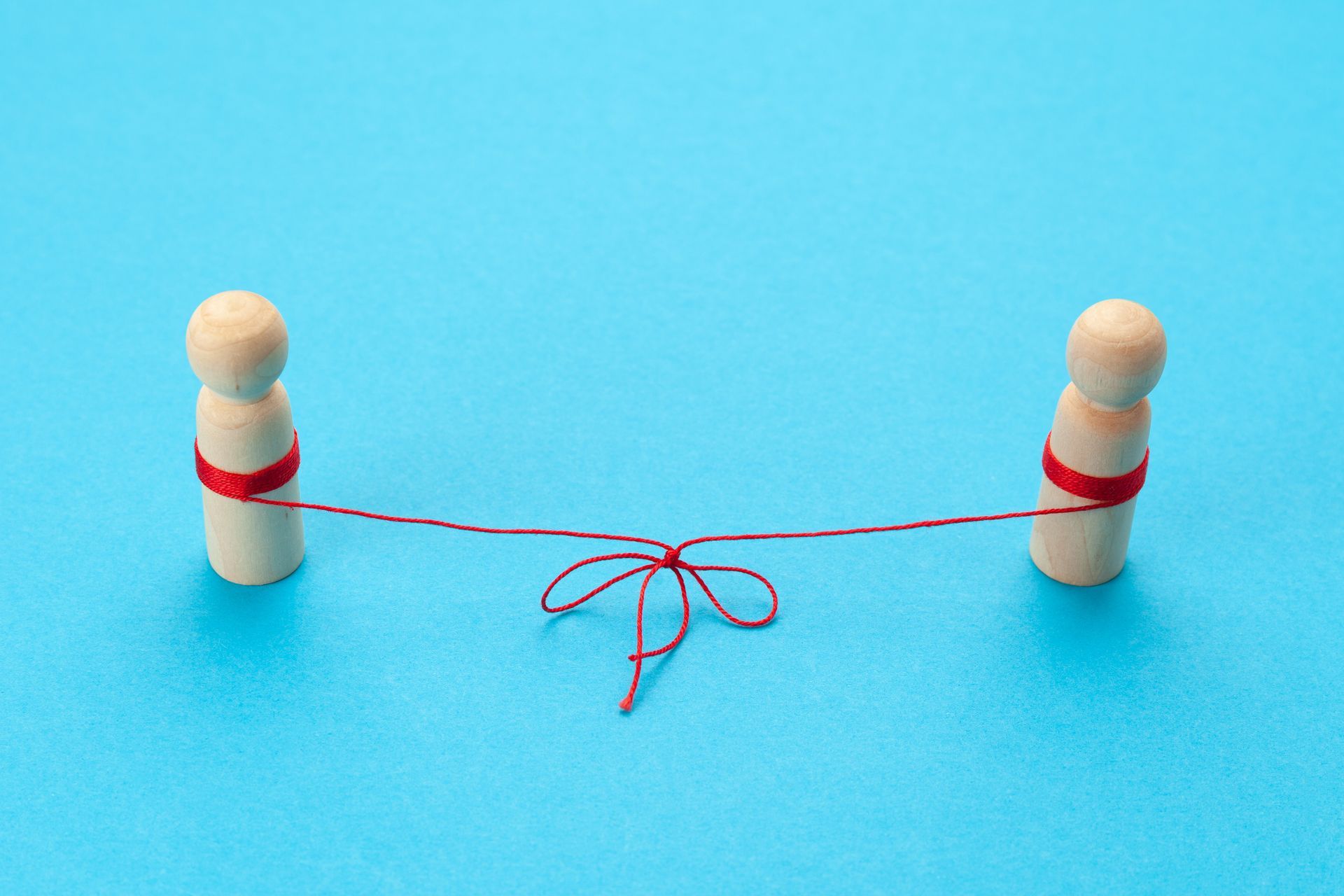 Two wooden pins linked by a red string tied in a bow on a blue background