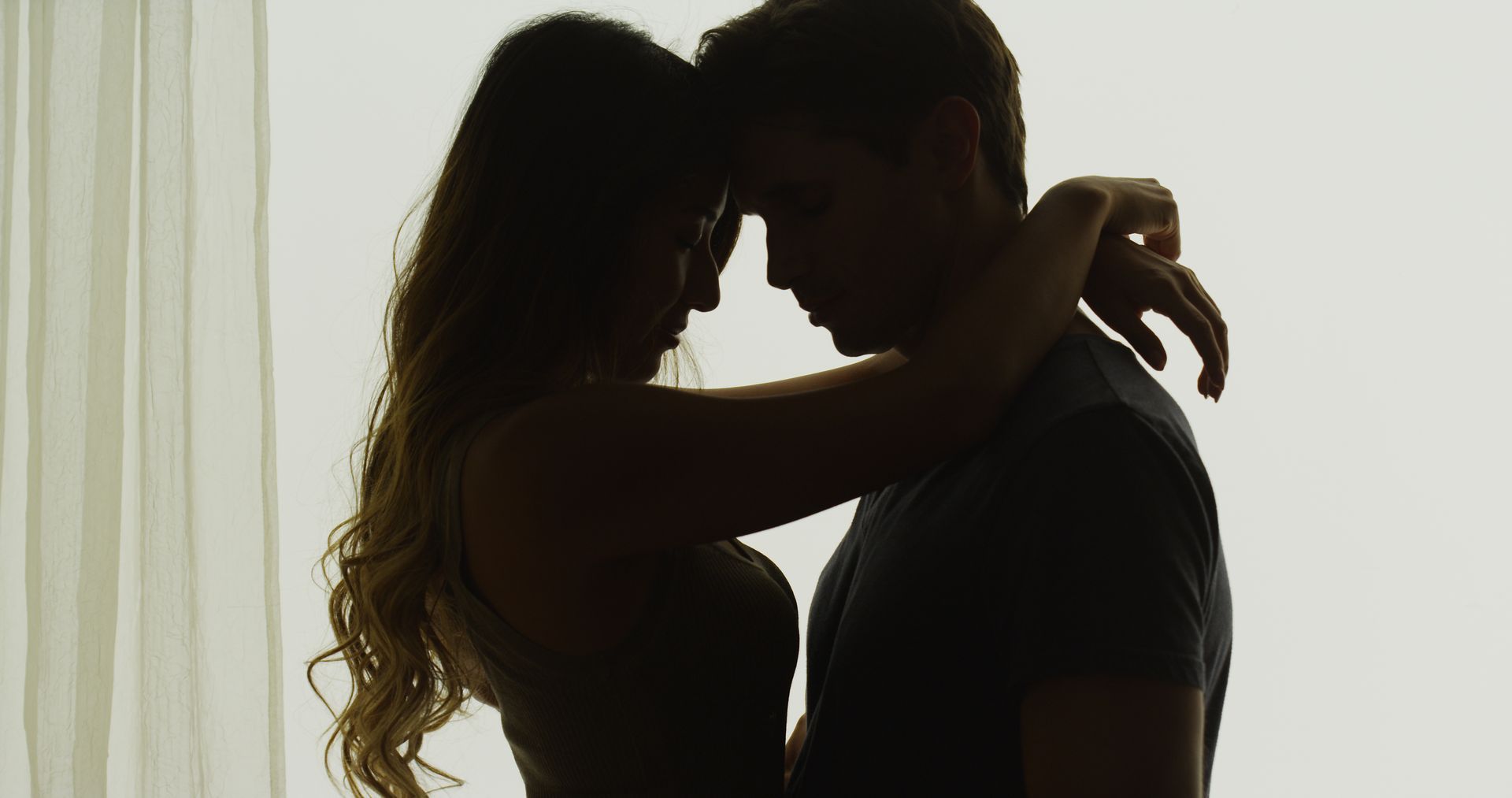 Silhouetted couple embracing closely against a bright backlit background.