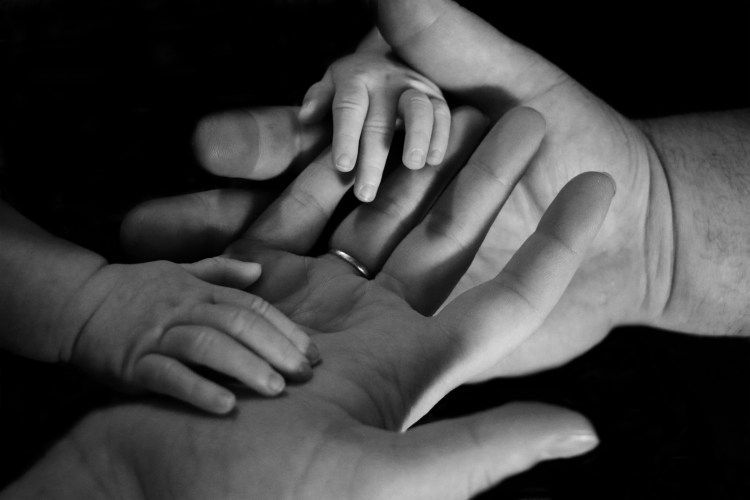 Black-and-white close-up of several hands stacked together in a gesture of support and unity