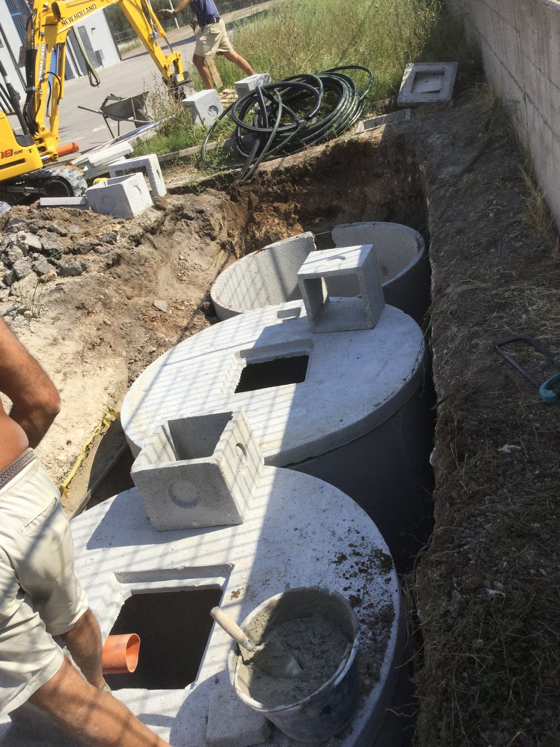 Installazione di serbatoi di cemento in una trincea, alla presenza di operai e attrezzature edili.