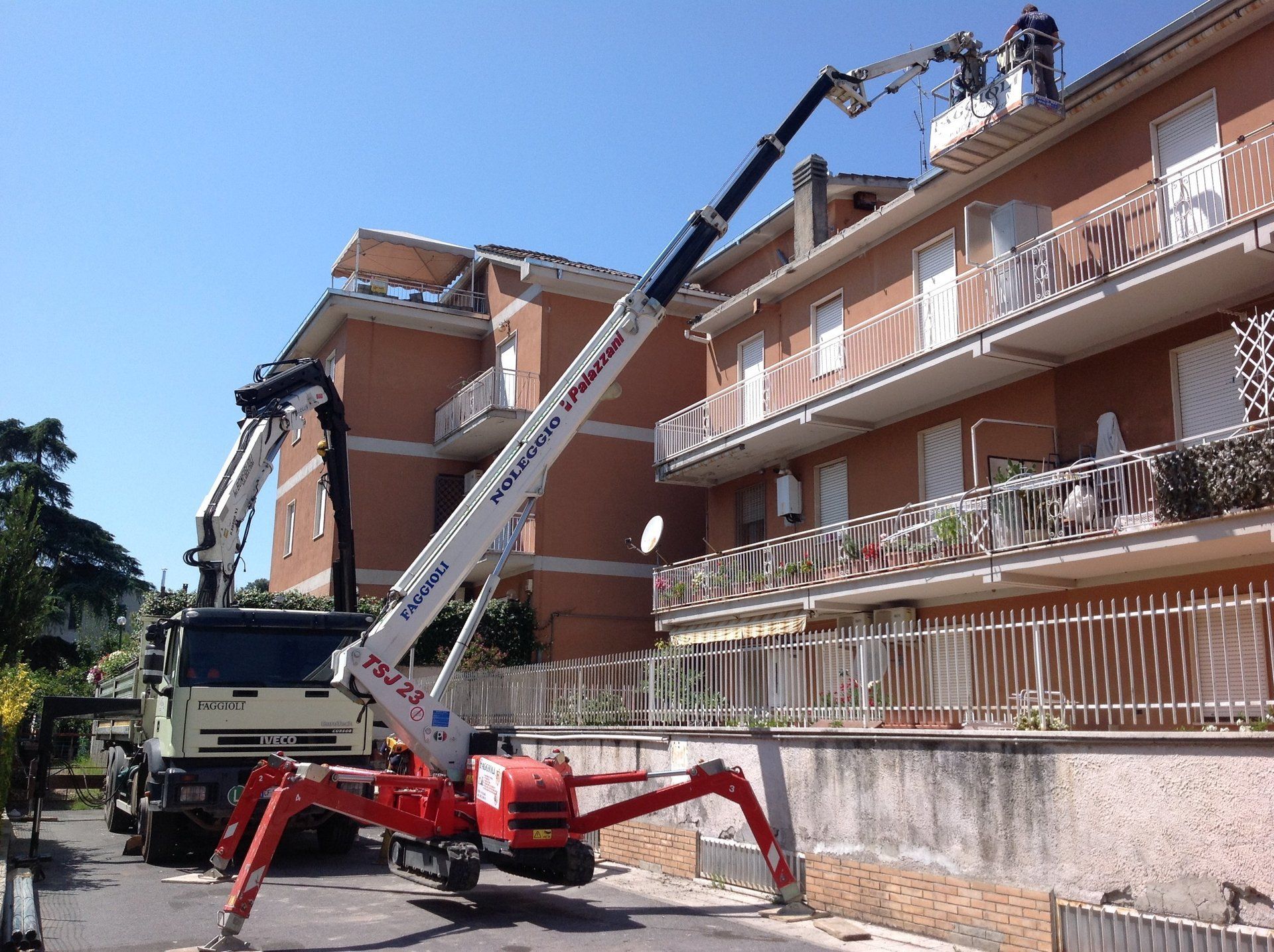 Una gru mobile solleva una piattaforma verso un edificio. Gli operai sono in piedi sulla piattaforma.