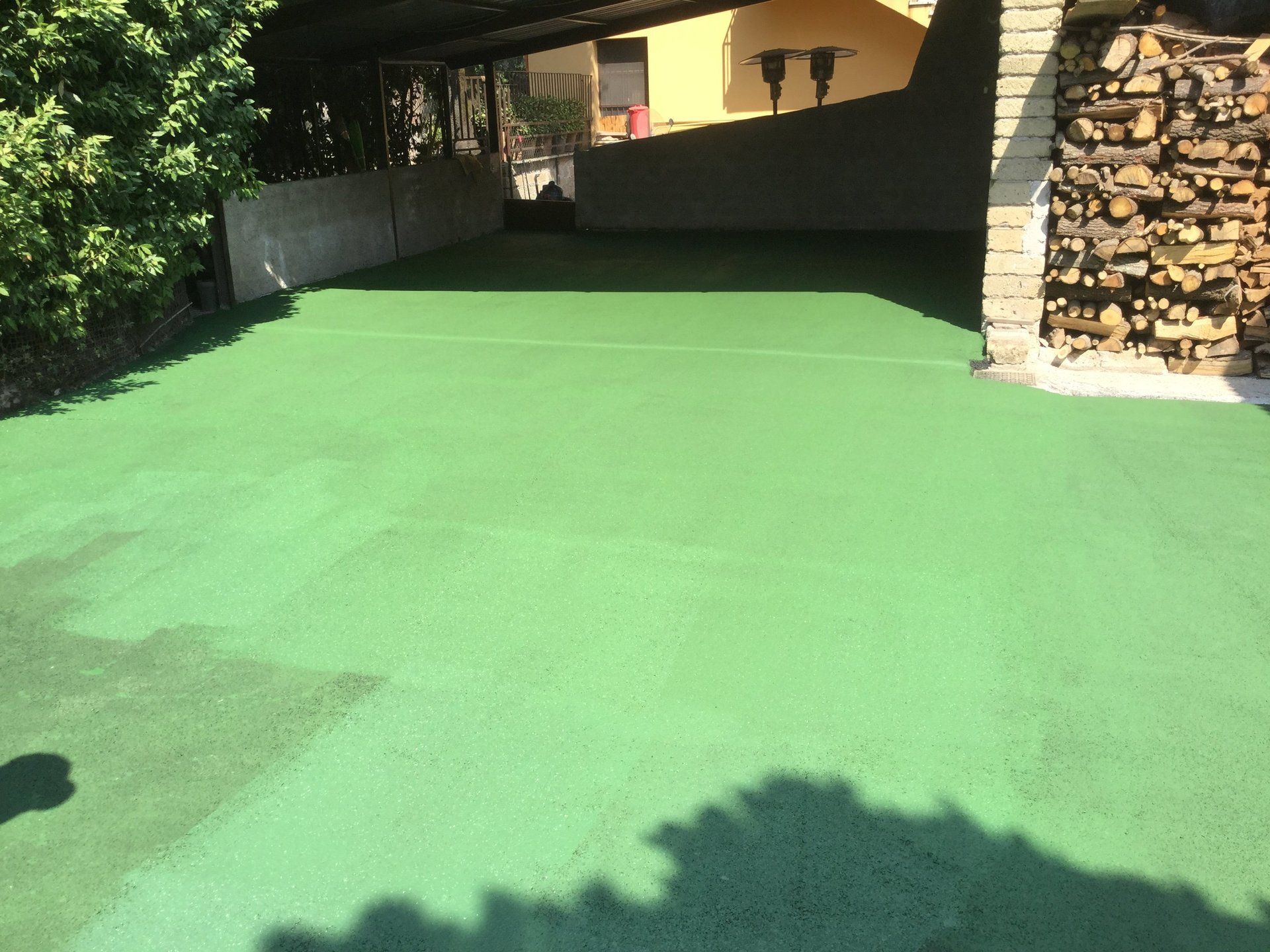 Vialetto d'accesso dipinto di verde con posto auto coperto e catasta di legna.