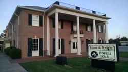 Brick funeral home building with white columns and a sign in front.