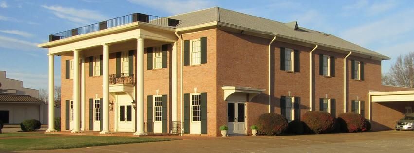 Two-story brick office building with white columns and a parking lot in front