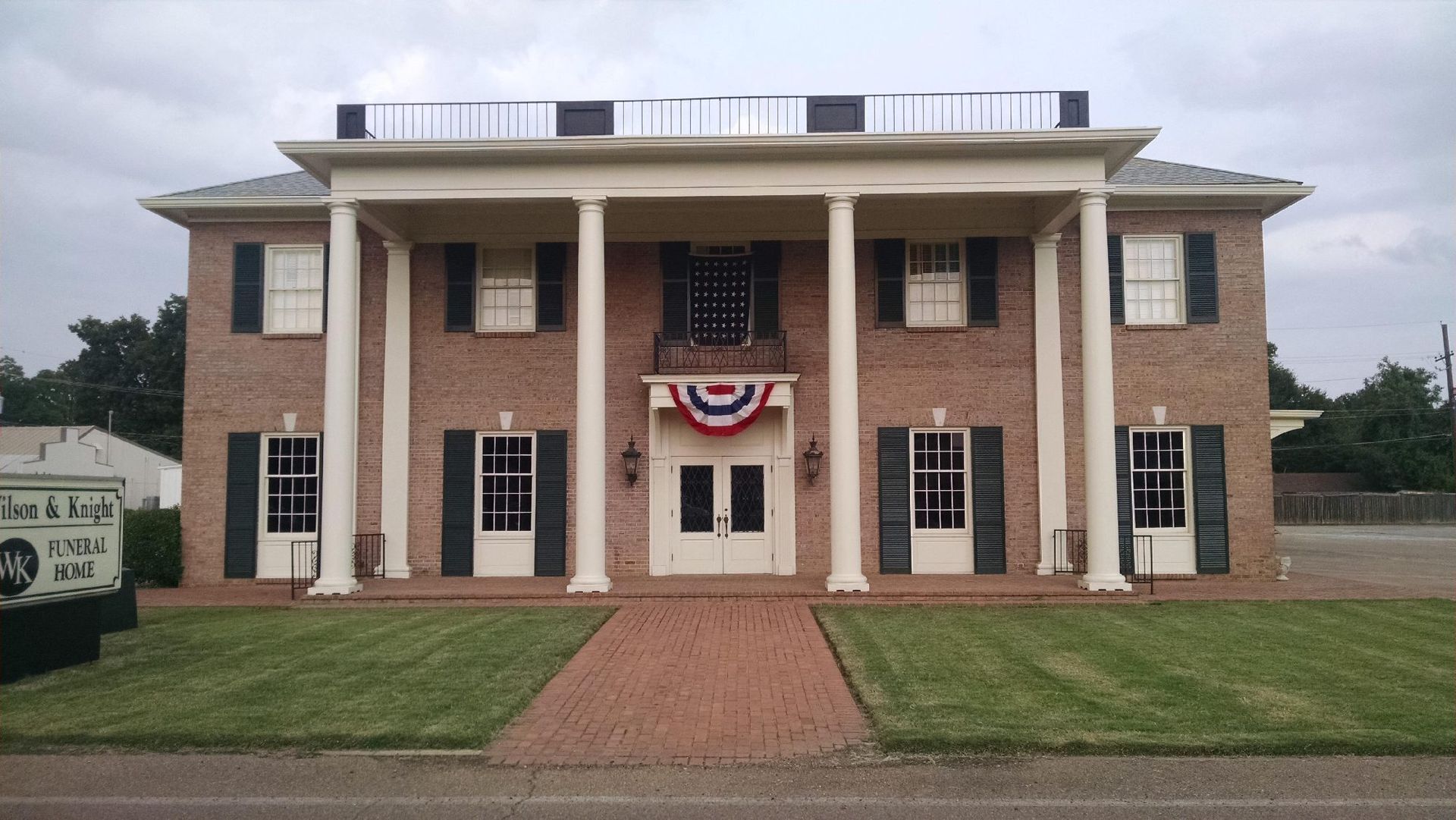 Brick civic building with white columns, red-white-blue bunting above the entrance, and a brick walkway