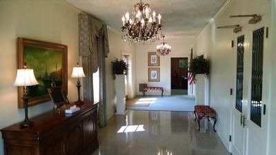 Elegant hallway with chandelier, marble floor, wooden sideboard, lamps, and framed art.
