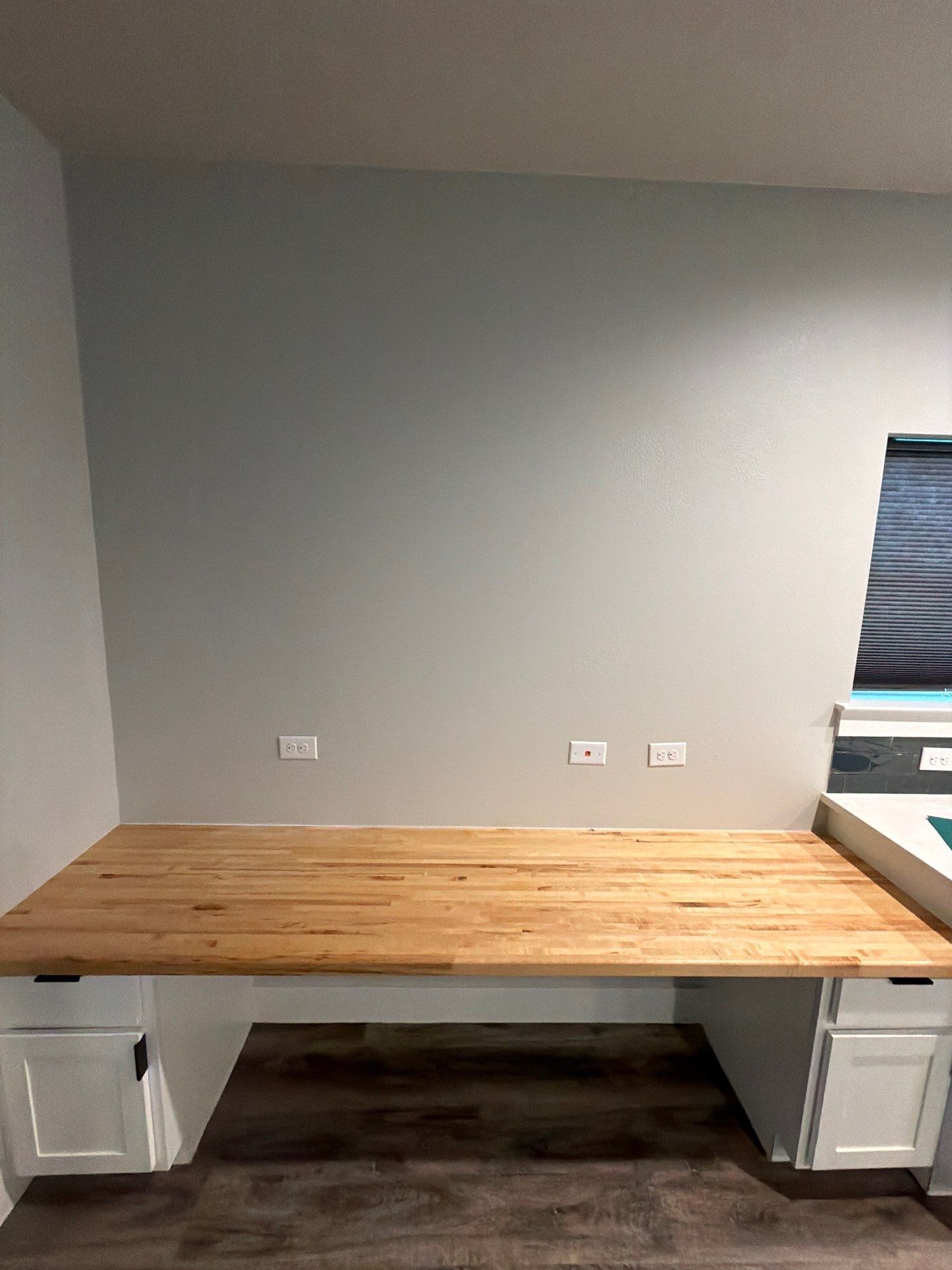 Wooden desk against a gray wall with outlets beneath a window nook