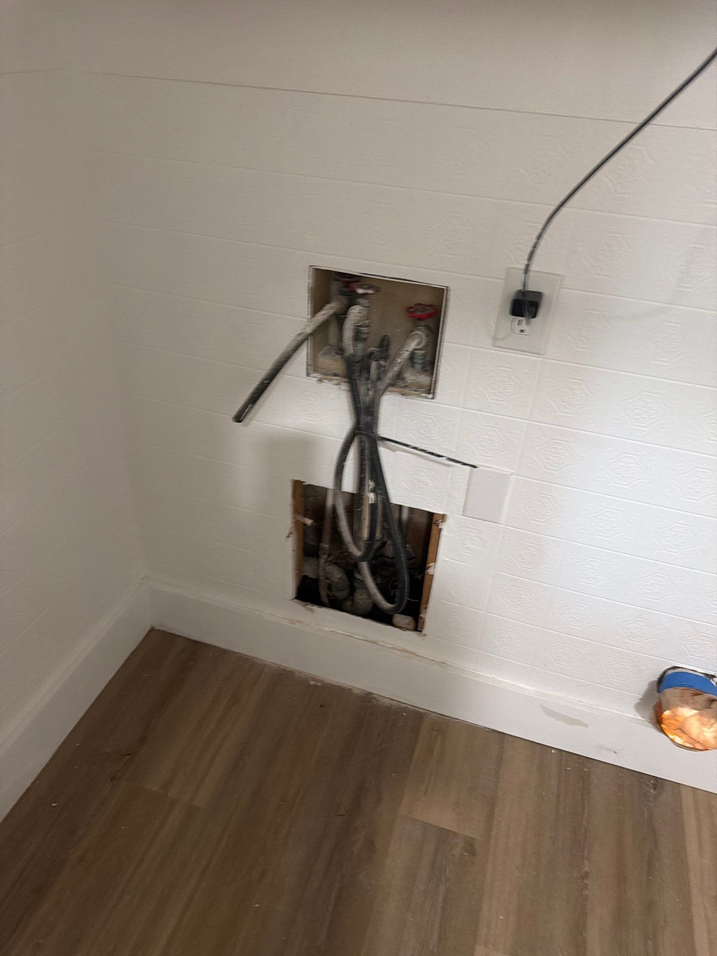 Open wall with exposed electrical wiring and cutouts above wood flooring in a mostly empty room