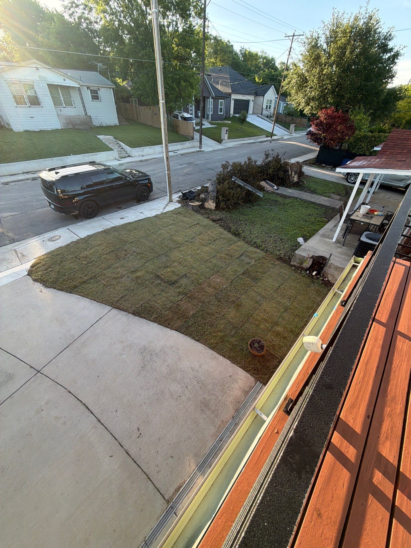 Front yard and driveway beside a street, with a garbage bin, trimmed lawn, and brick porch steps at right.