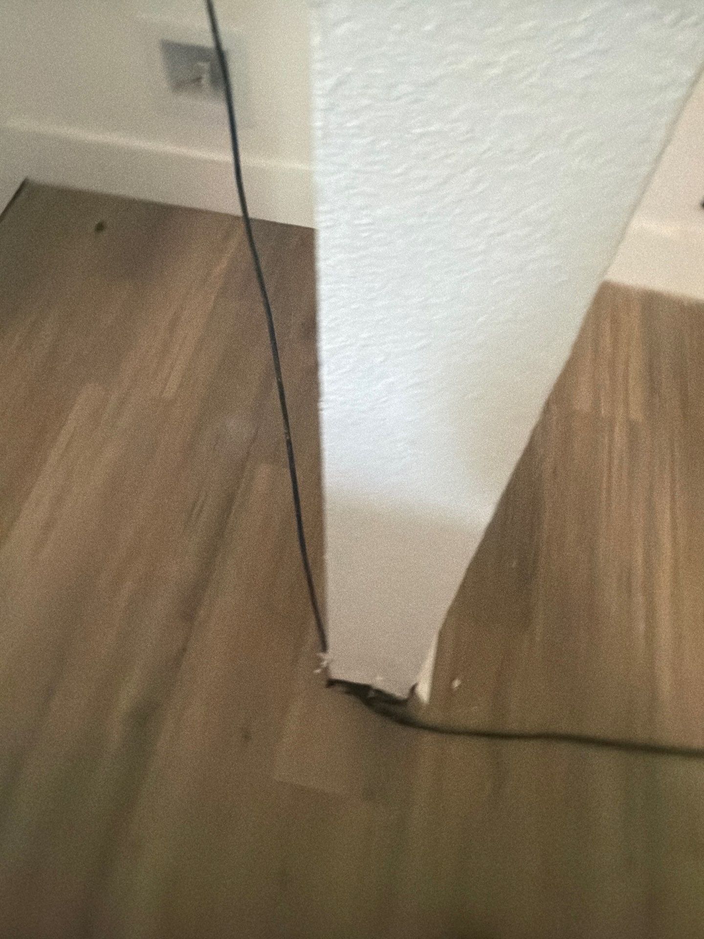 Black cable runs along a wood floor beside a white wall corner.