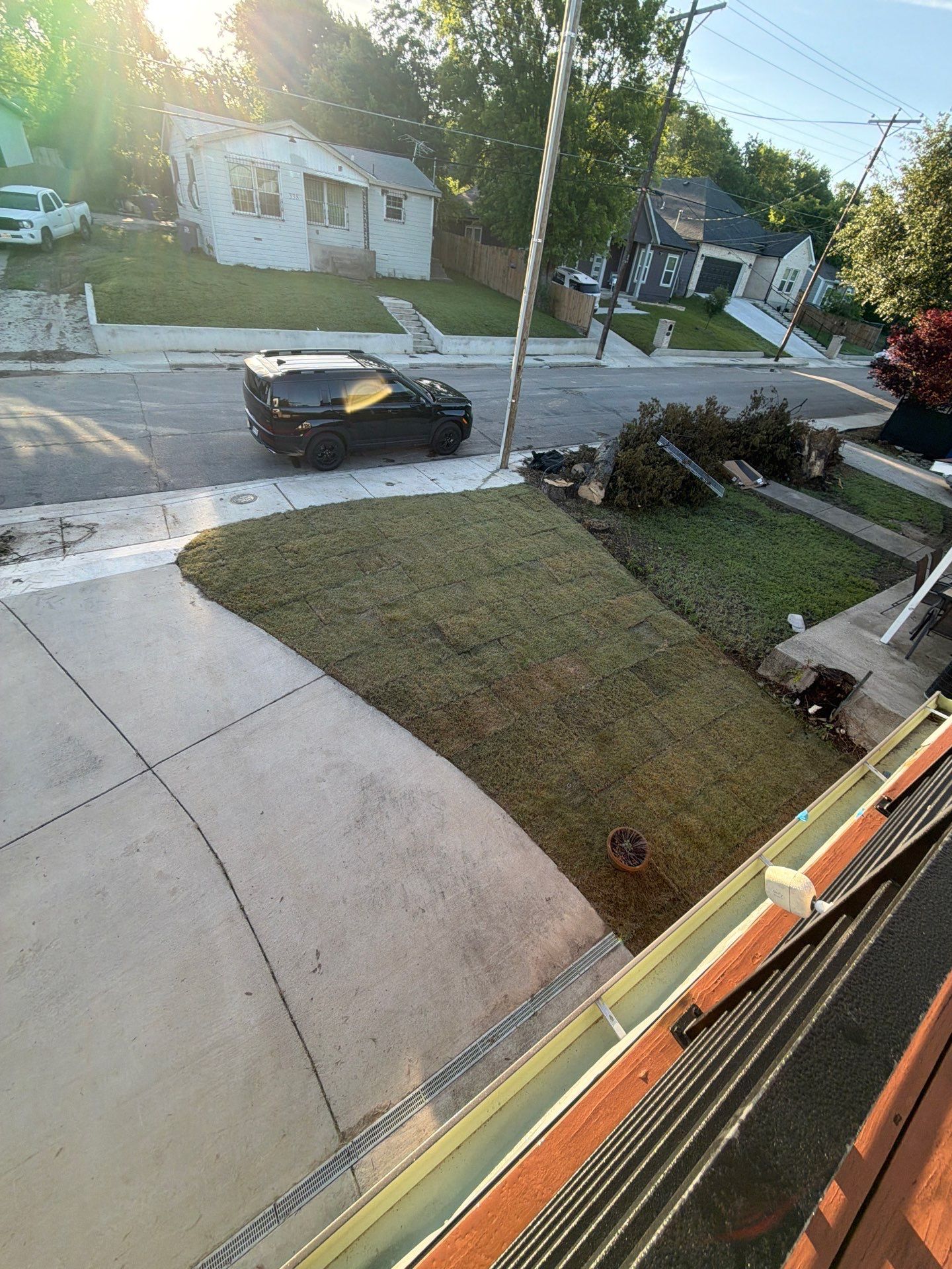 Front porch view of a quiet suburban street with a parked black car, lawns, and a sunlit house across the road