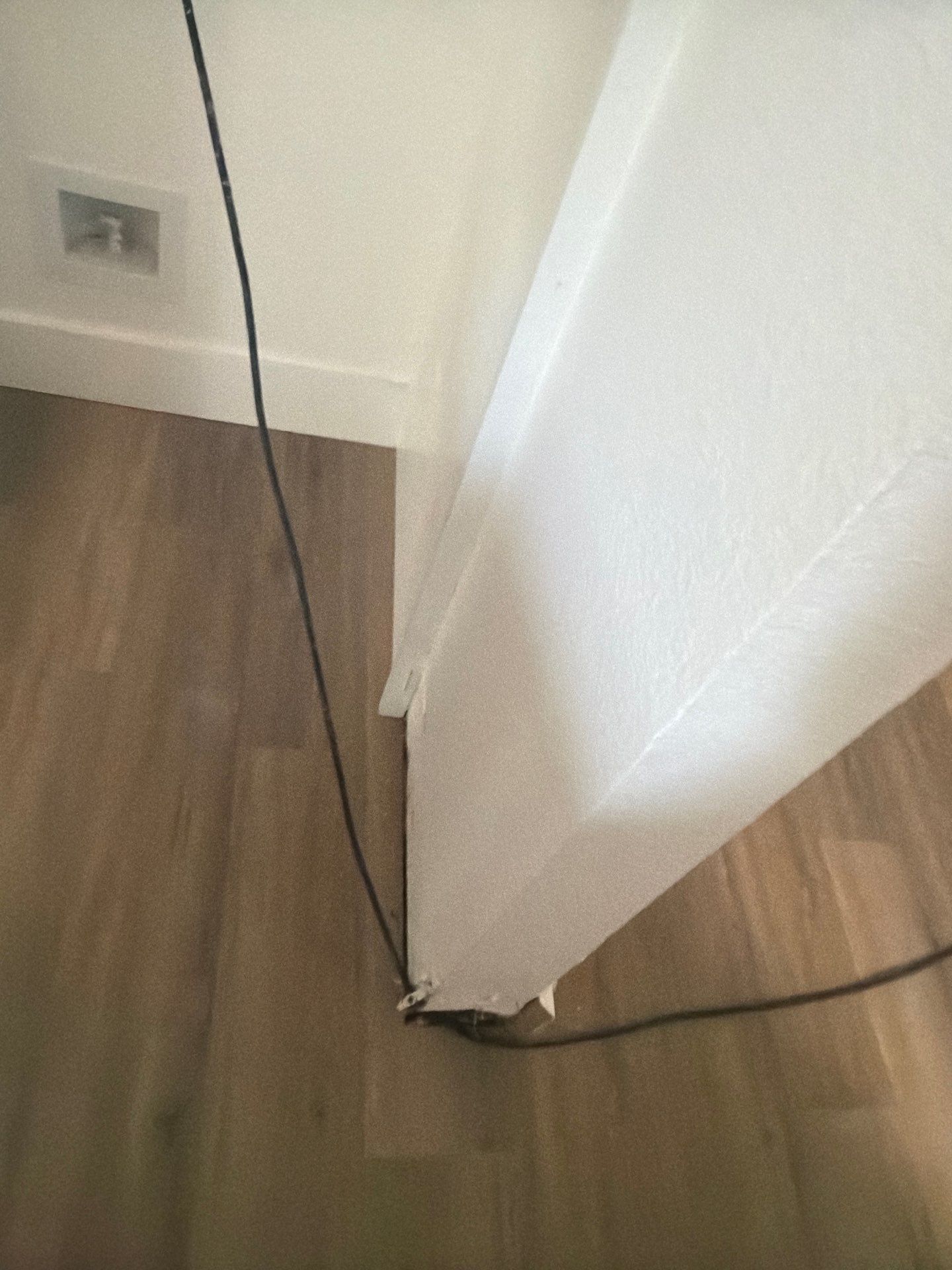 Corner of a room with wood floor, white wall, and black cable running along the baseboard.