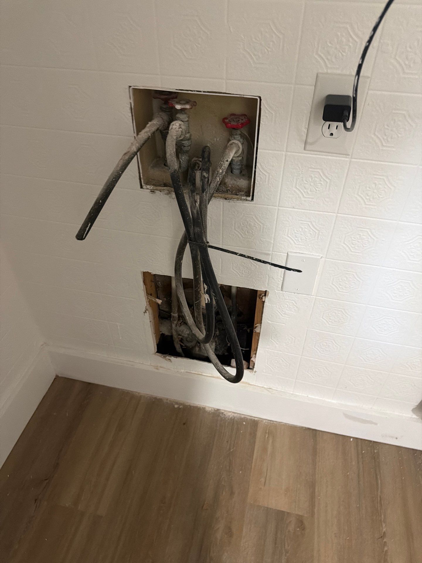 Open wall electrical boxes with exposed cables and outlets in a room with wood flooring.