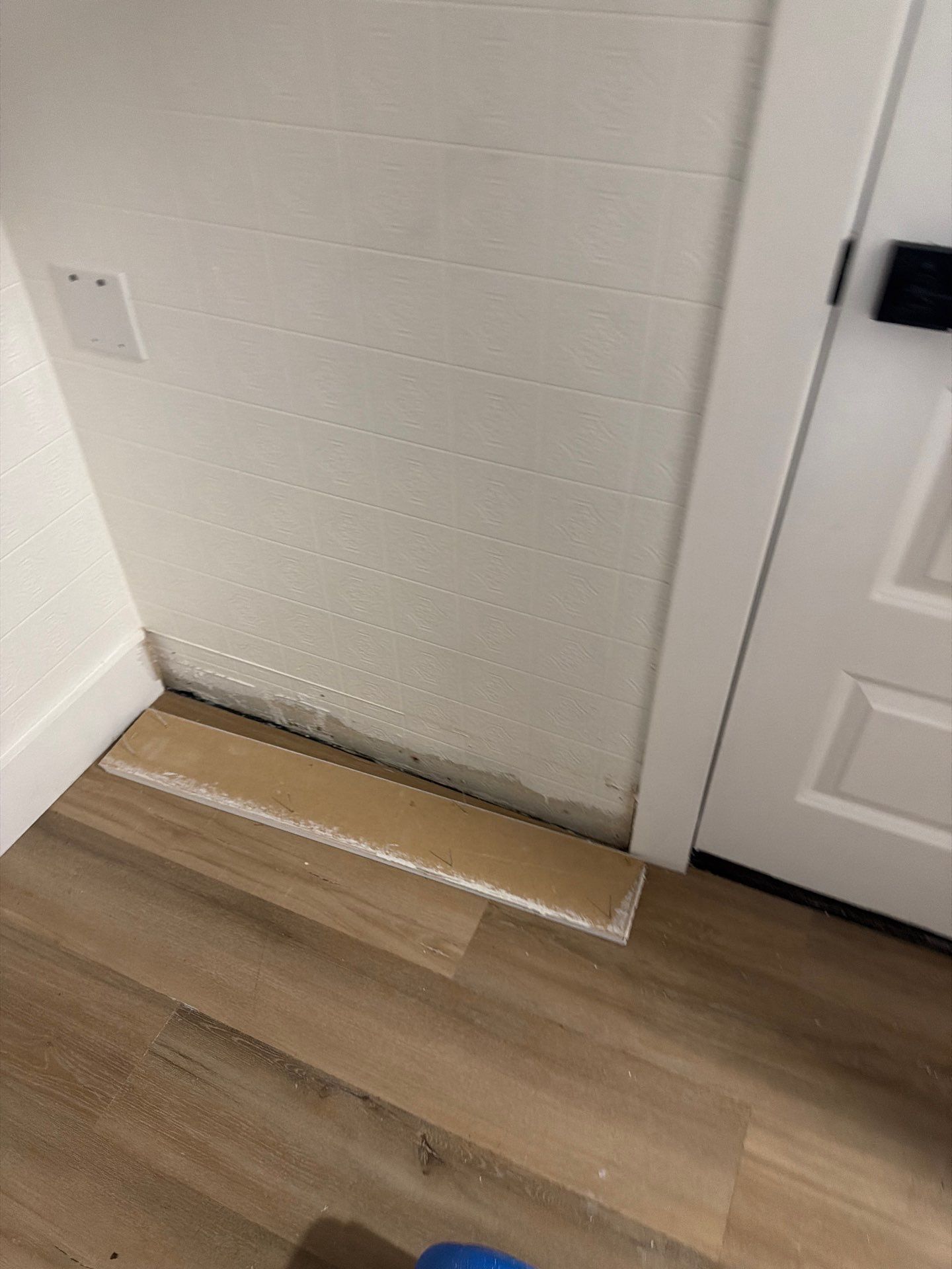 Wooden board leaning against a white wall beside a door on a wood floor