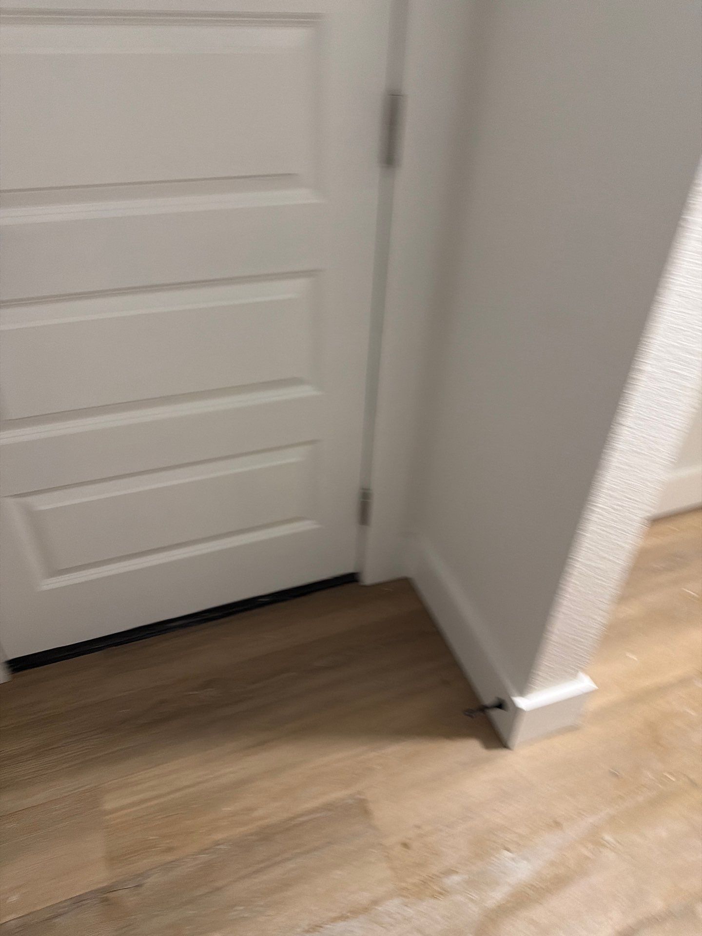 White interior door with a black doorstop beside a light wood floor and white wall corner.