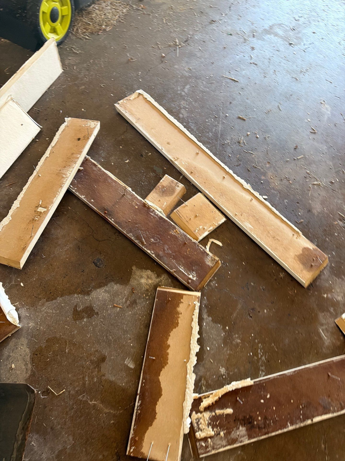 Scattered wooden boards with worn edges on a wet concrete floor in a garage or workshop