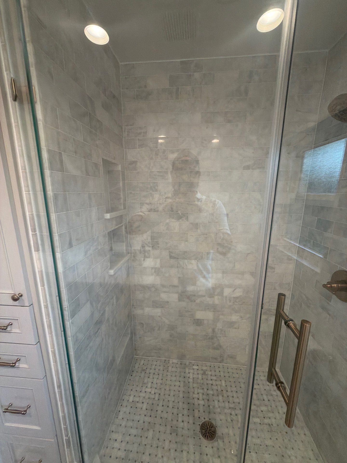 Empty tiled walk-in shower with glass door and chrome handle.