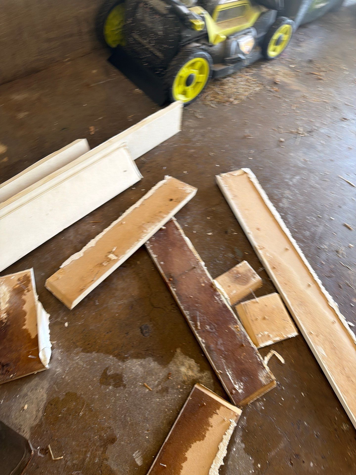 Scattered wooden boards on a wet garage floor beside a black-and-yellow toy vehicle.