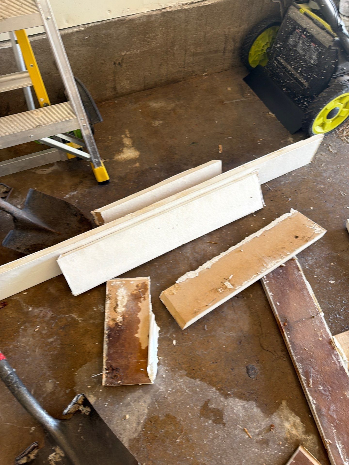 Scattered wooden boards and debris on a wet floor beside a wall and cart