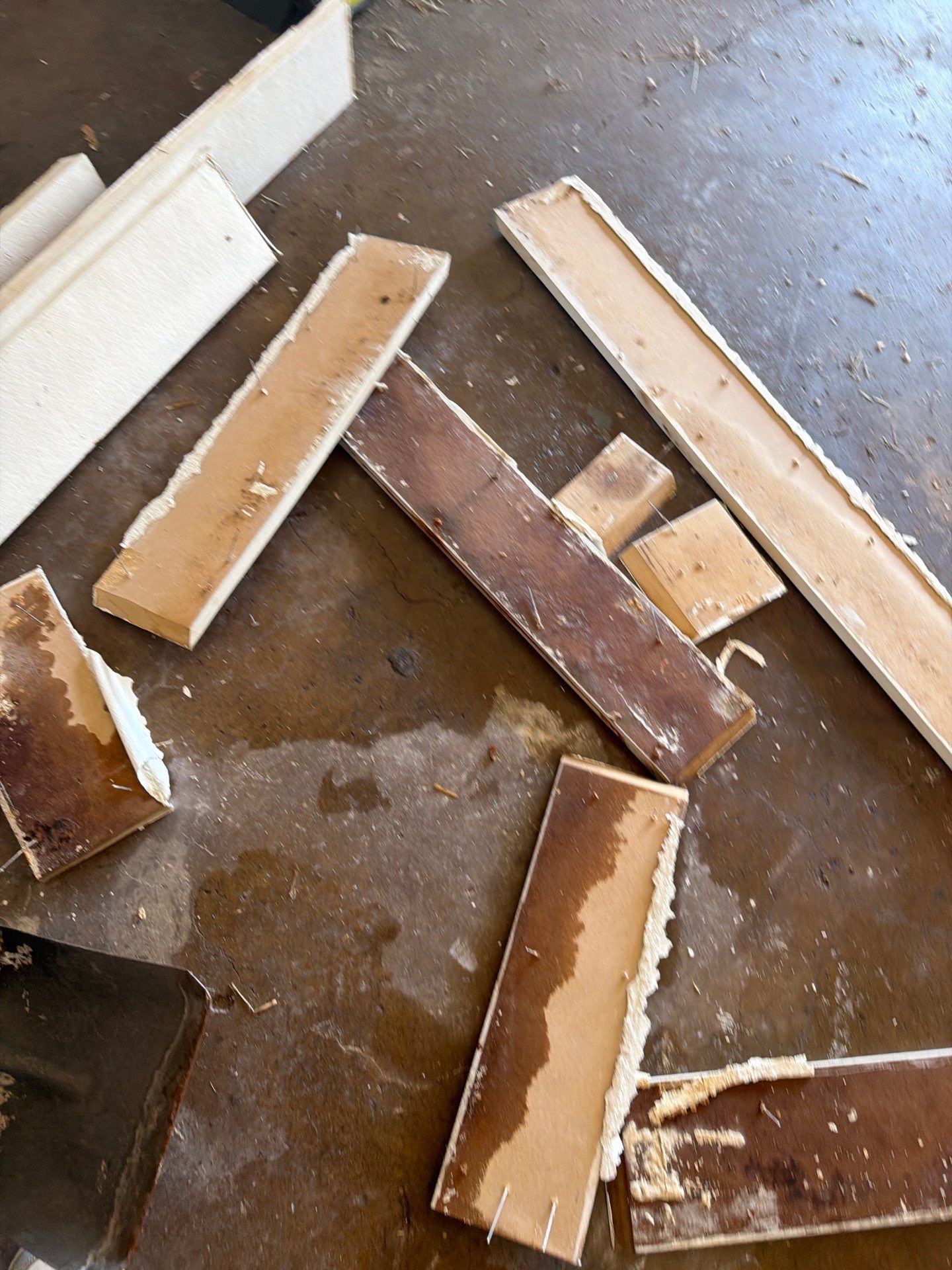 Scattered broken wooden boards and white debris on a concrete floor with a dark tool at the edge
