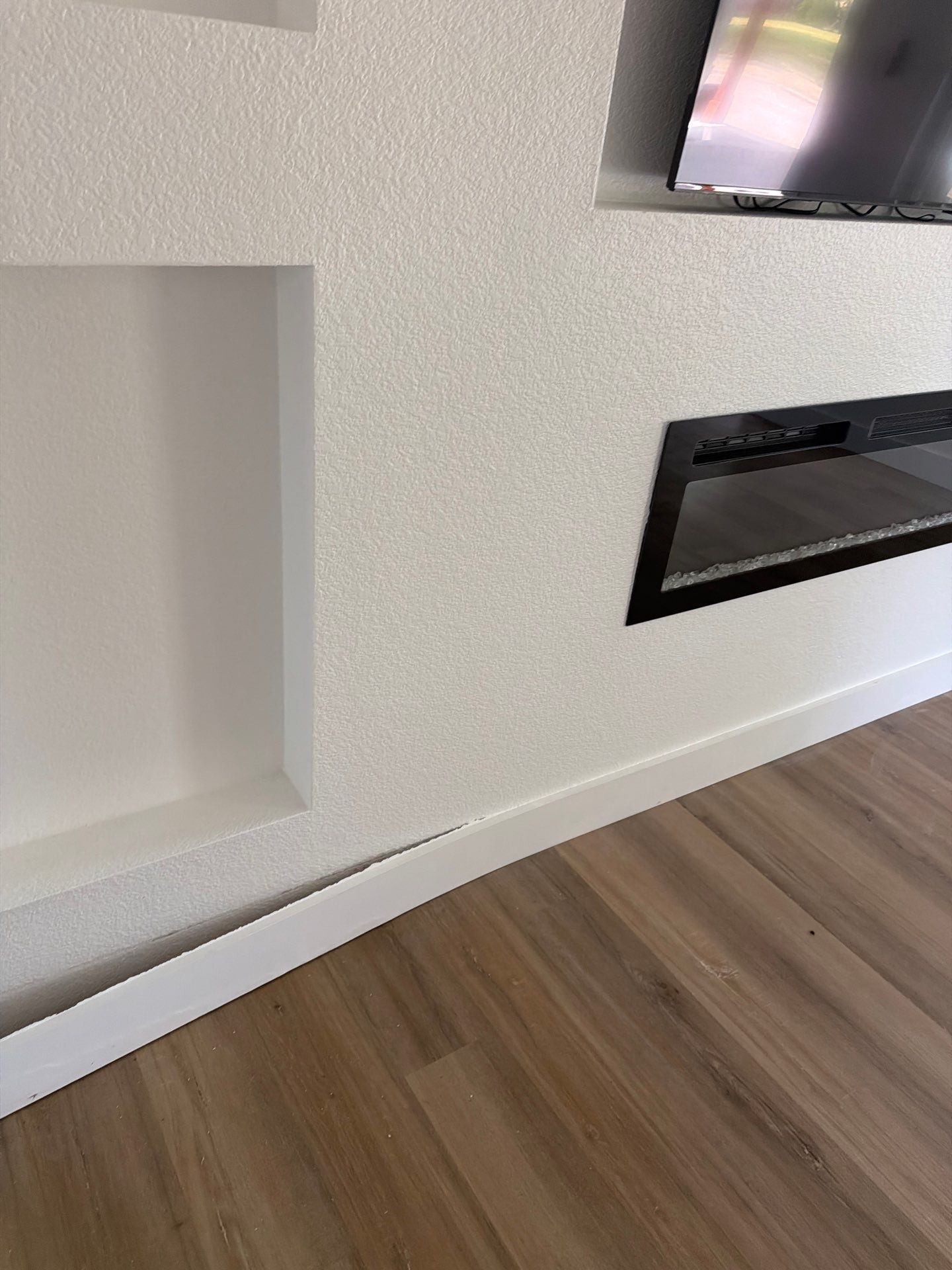 Living room wall with recessed niche, wall-mounted TV, and black fireplace over wood flooring
